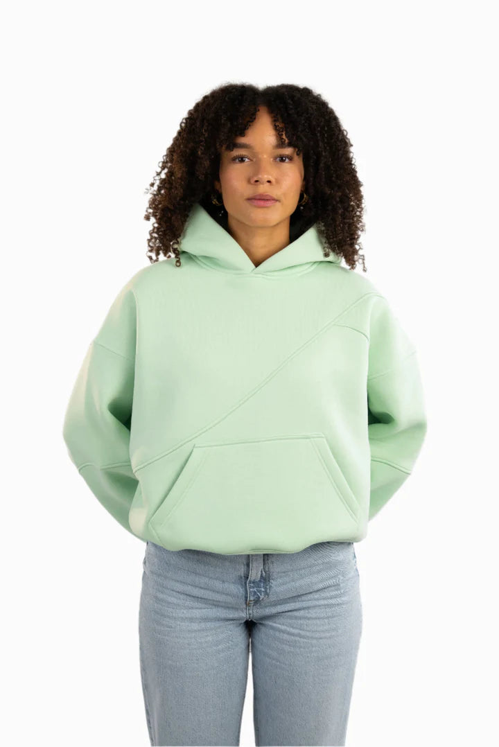 Mintgrüner Hoodie mit diagonalen Ziernähten auf der Vorderseite, getragen von einem weiblichen Model.
