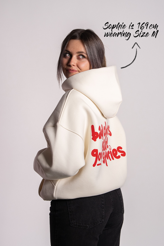 Nahaufnahme von Sophie, die einen cremefarbenen Hoodie trägt. Der Blick ist über die Schulter nach hinten gerichtet. Auf dem Rücken steht in rotem, verspieltem Schriftzug: „bad choices make good stories“. Sophie ist 169 cm groß und trägt Größe M.