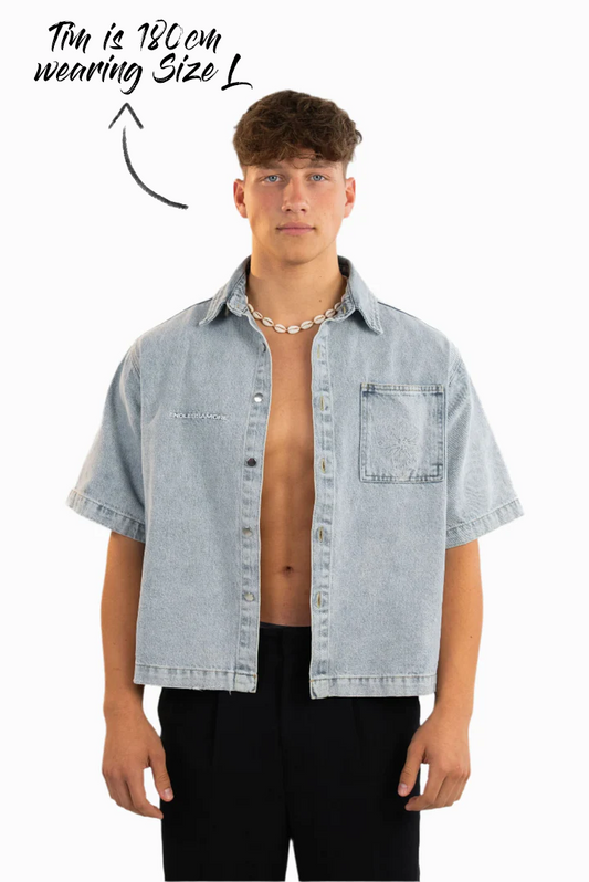 Kurzärmeliges Jeanshemd in hellem Waschton mit aufgesticktem weißen „ENDLESSAMORE“-Logo auf der linken Brust. Die Passform ist locker, das Hemd wird offen getragen.