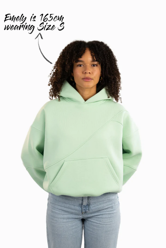 Mintgrüner Hoodie mit diagonalen Ziernähten auf der Vorderseite, getragen von einem weiblichen Model.