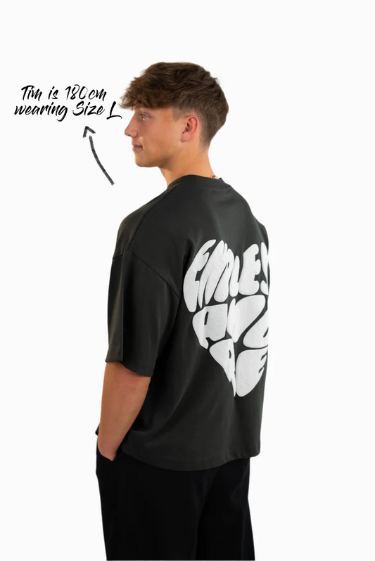 Schwarzes Oversized-T-Shirt mit großem weißen Rückendruck in Herzform und dem Schriftzug „ENDLESS AMORE“. Das Model (180 cm) trägt Größe L und steht seitlich mit Blick nach hinten.