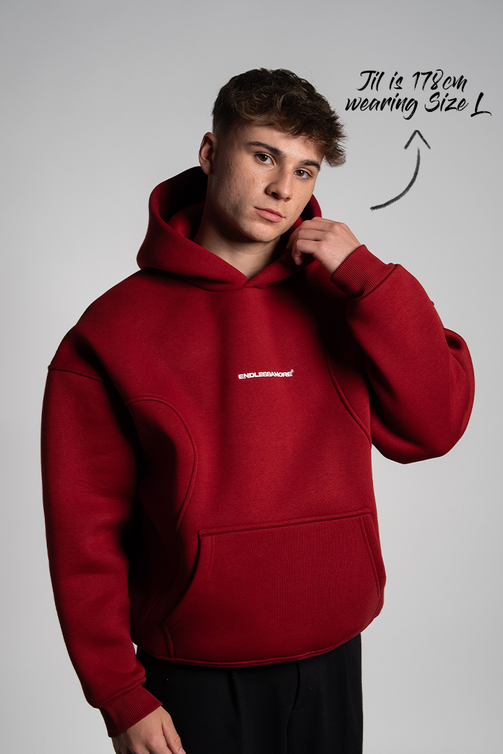 Mann mit kurzem Haar trägt einen bordeauxroten Hoodie mit zentral platziertem weißen „ENDLESSAMORE“-Brustprint. Der Hoodie hat betonte Nahtführung im Brustbereich.