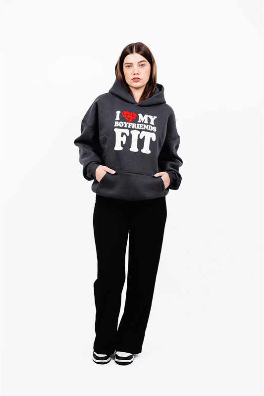 Dunkelgrauer Hoodie mit auffälligem weißen und roten Frontprint „I ❤️ MY BOYFRIENDS FIT“. Das Model steht frontal mit leicht angewinkelten Armen und Händen in den Taschen. Der Hoodie wirkt oversized und gemütlich.