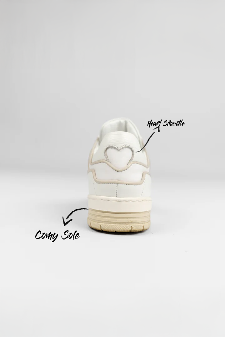 Hintere Studioansicht eines weißen Sneakers mit beige abgesetzten Nähten. Auf der Ferse ist eine dekorative Herz-Silhouette eingearbeitet. Die handschriftlichen Anmerkungen im Bild verweisen auf eine bequeme Sohle.