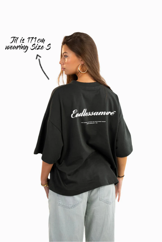 Rückansicht des schwarzen T-Shirts mit weißem Rückendruck „Endlessamore™“ und kleinem Text darunter. Oben links steht „Jil is 171 cm wearing Size S“.