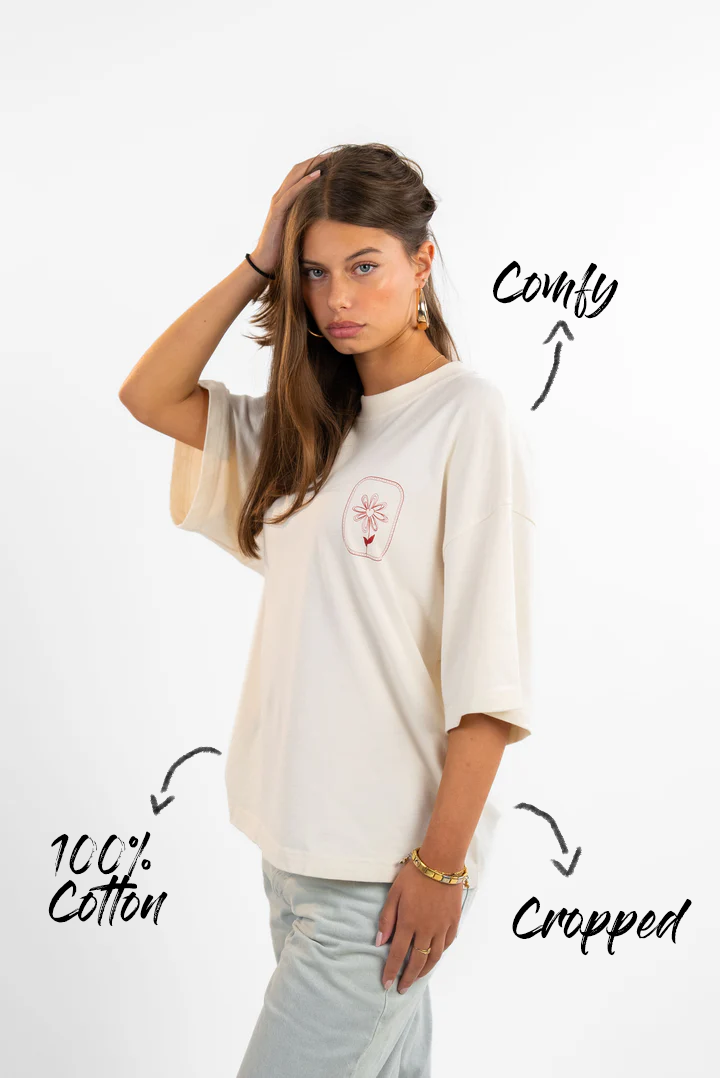 Seitenansicht eines weißen T-Shirts mit floraler Bruststickerei und weitem Schnitt. Beschriftungen heben Material (100 % Baumwolle) und Tragekomfort hervor.