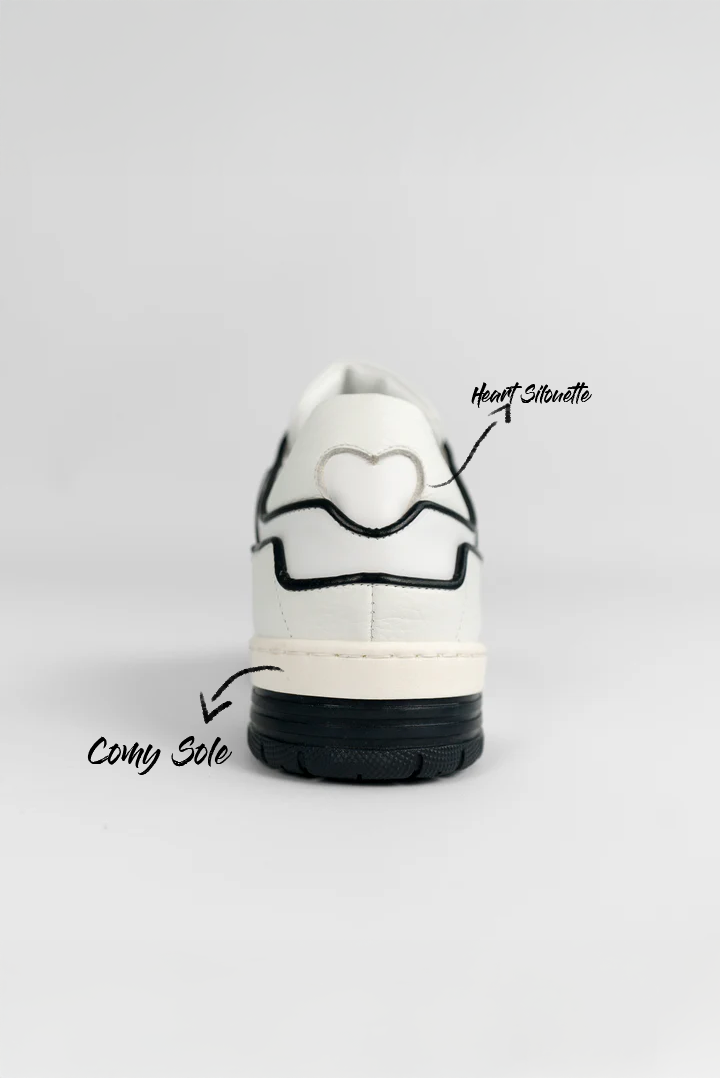 Rückansicht eines weißen Sneakers mit schwarzer Kontur und gestickter Herzform im Fersenbereich. Die Sohle ist zweifarbig in Beige und Schwarz gestaltet.