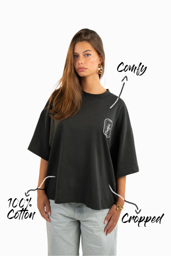 Vorderansicht des schwarzen T-Shirts mit lockerem, leicht cropped Schnitt. Der weiße Brustprint zeigt ein kleines Baum-Motiv. Beschriftet mit „Comfy“, „Cropped“ und „100% Cotton“.