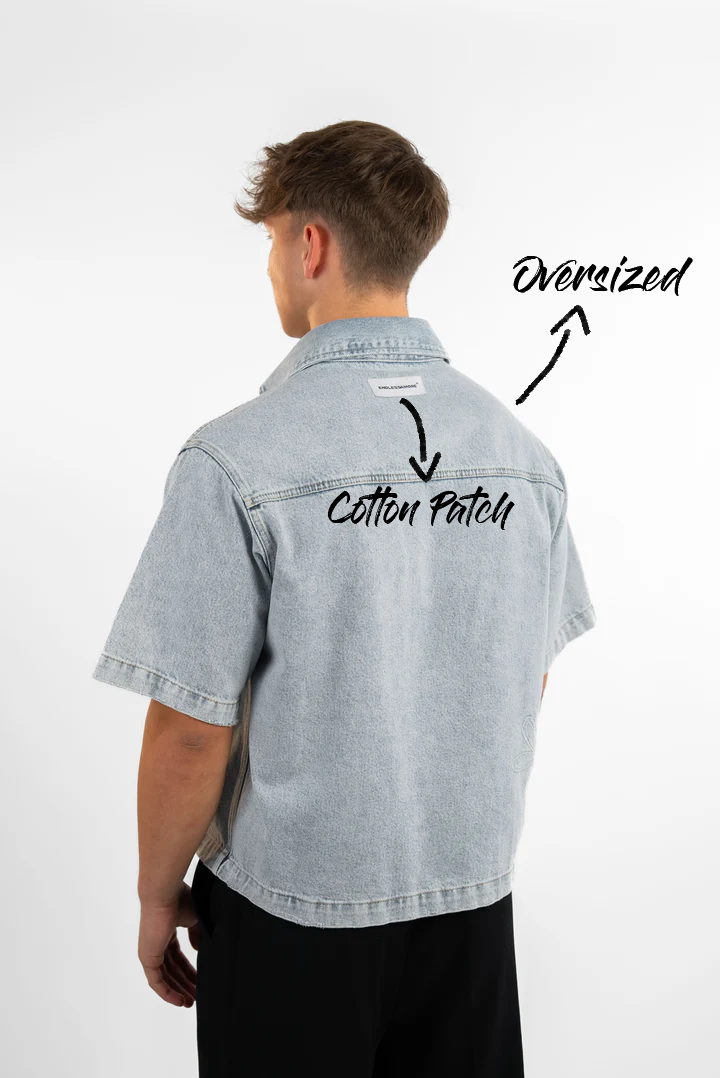 Locker geschnittenes Jeanshemd in hellblauer Waschung, Rückansicht mit Etikett auf Schulterhöhe. Die Passform ist oversized und endet auf Hüfthöhe.