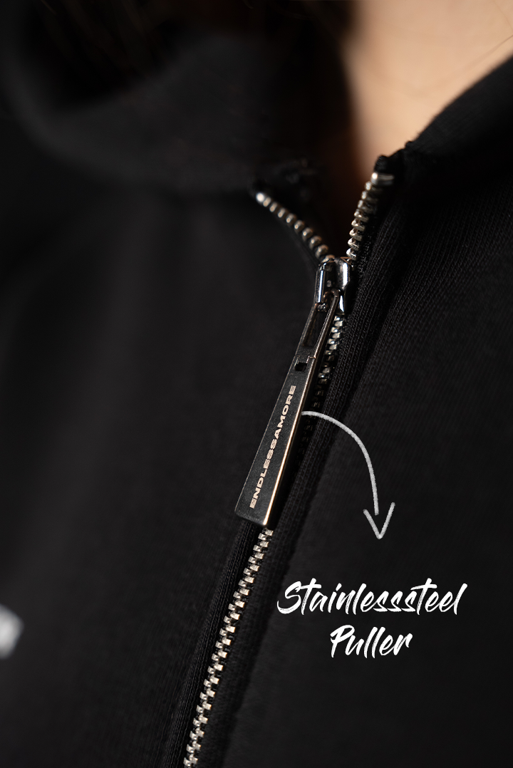 Nahaufnahme des silberfarbenen Edelstahl-Zippers des schwarzen Hoodies. Der Zipper trägt die Gravur „ENDLESSAMORE“.