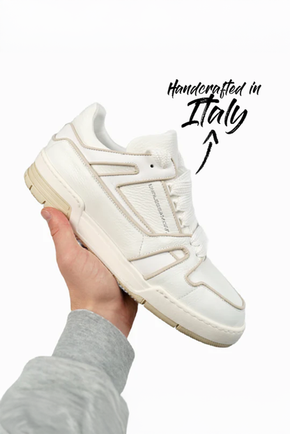 Ein weiß-beiger Sneaker wird von einer Hand mit grauem Ärmel hochgehalten. Auf dem seitlichen Obermaterial ist das Markenlogo “ENDLESSAMORE” zu erkennen. Eine handschriftliche Beschriftung im Bild weist auf die italienische Handarbeit des Schuhs hin.