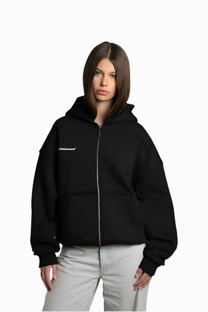 Jil trägt einen schwarzen Zip-Hoodie mit weißem Brustprint „ENDLESSAMORE®“. Die Kapuze ist locker aufgesetzt, der Reißverschluss ist geschlossen. Der Hoodie ist cropped geschnitten und hat sichtbare Teilungsnähte.
