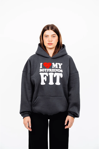 Dunkelgrauer Hoodie mit weißem Frontprint „I ❤️ MY BOYFRIENDS FIT“ und rotem Herz mit Schriftzug „ENDLESS AMORE“. Der Hoodie hat eine Kängurutasche und wird locker getragen. Vorderansicht, das Model steht gerade mit herabhängenden Armen.