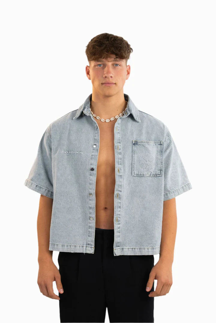 Kurzärmeliges Jeanshemd in hellem Waschton mit aufgesticktem weißen „ENDLESSAMORE“-Logo auf der linken Brust. Die Passform ist locker, das Hemd wird offen getragen.