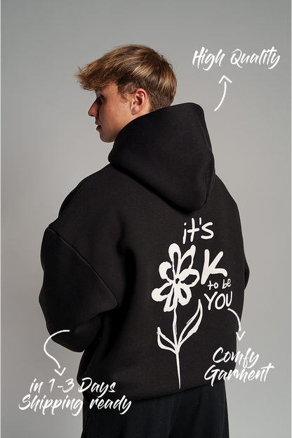 Rückseite eines schwarzen Hoodies mit großem, weißen Puffprint: stilisierte Blume mit Schriftzug „it’s OK to be YOU“.