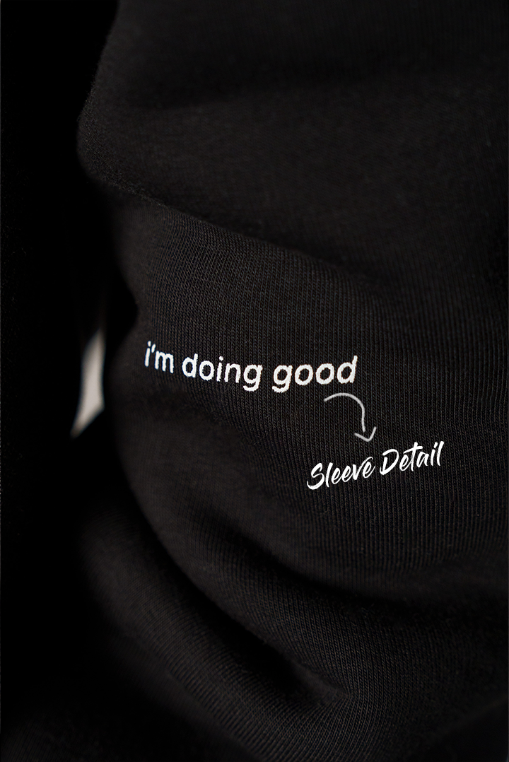 Nahaufnahme des schwarzen Ärmels mit kleinem weißem Print. Der Text lautet „i’m doing good“, daneben steht grafisch markiert „Sleeve Detail“.
