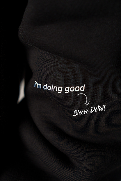 Nahaufnahme des schwarzen Ärmels mit kleinem weißem Print. Der Text lautet „i’m doing good“, daneben steht grafisch markiert „Sleeve Detail“.

