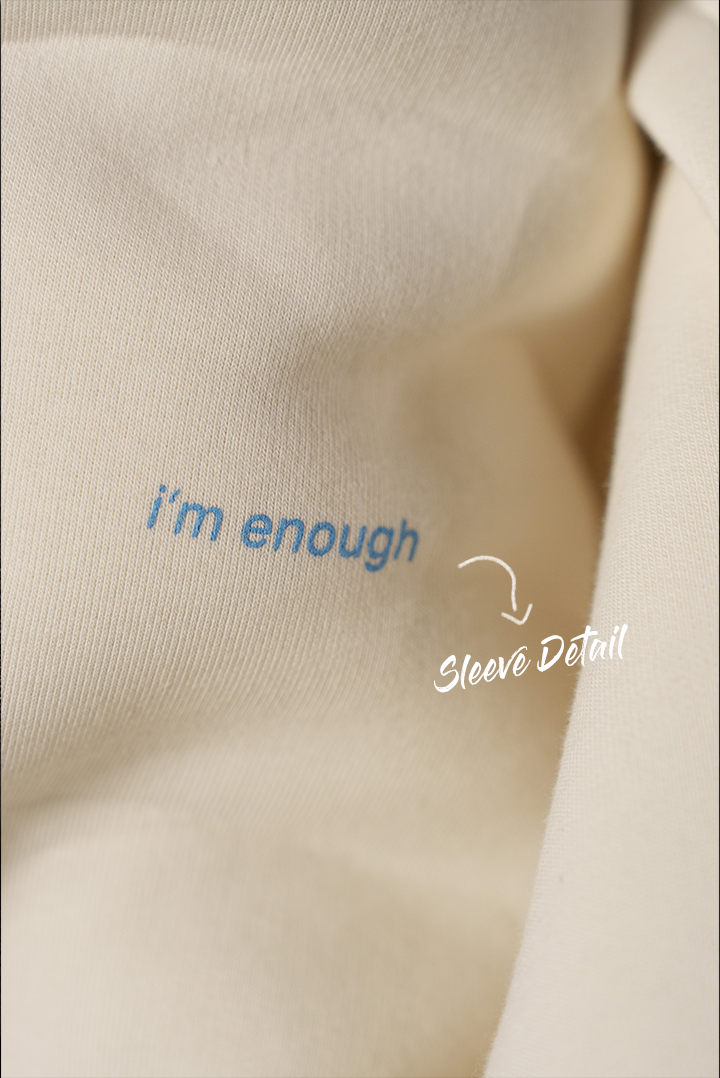 Detailaufnahme des Ärmels eines weißen Hoodies mit hellblauem Schriftzug „i’m enough“.