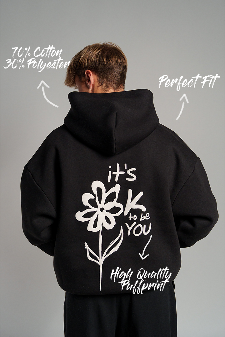 Schwarzer Kapuzenpullover mit großem weißen Rückendruck. Der Print zeigt eine stilisierte Blume mit dem Schriftzug „it’s OK to be YOU“. Darüber sind die Hinweise „70 % Cotton / 30 % Polyester“, „Perfect Fit“ und „High Quality Puffprint“ grafisch eingefügt.