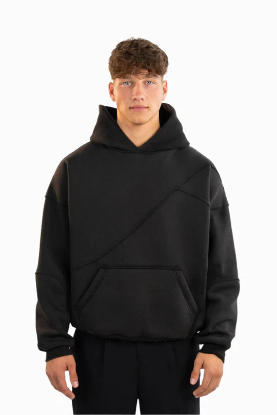Schwarzer Kapuzenpullover mit sichtbaren Teilungsnähten und Kängurutasche, getragen von einem Model. Der Hoodie hat eine lockere Passform und eine strukturierte Oberfläche.