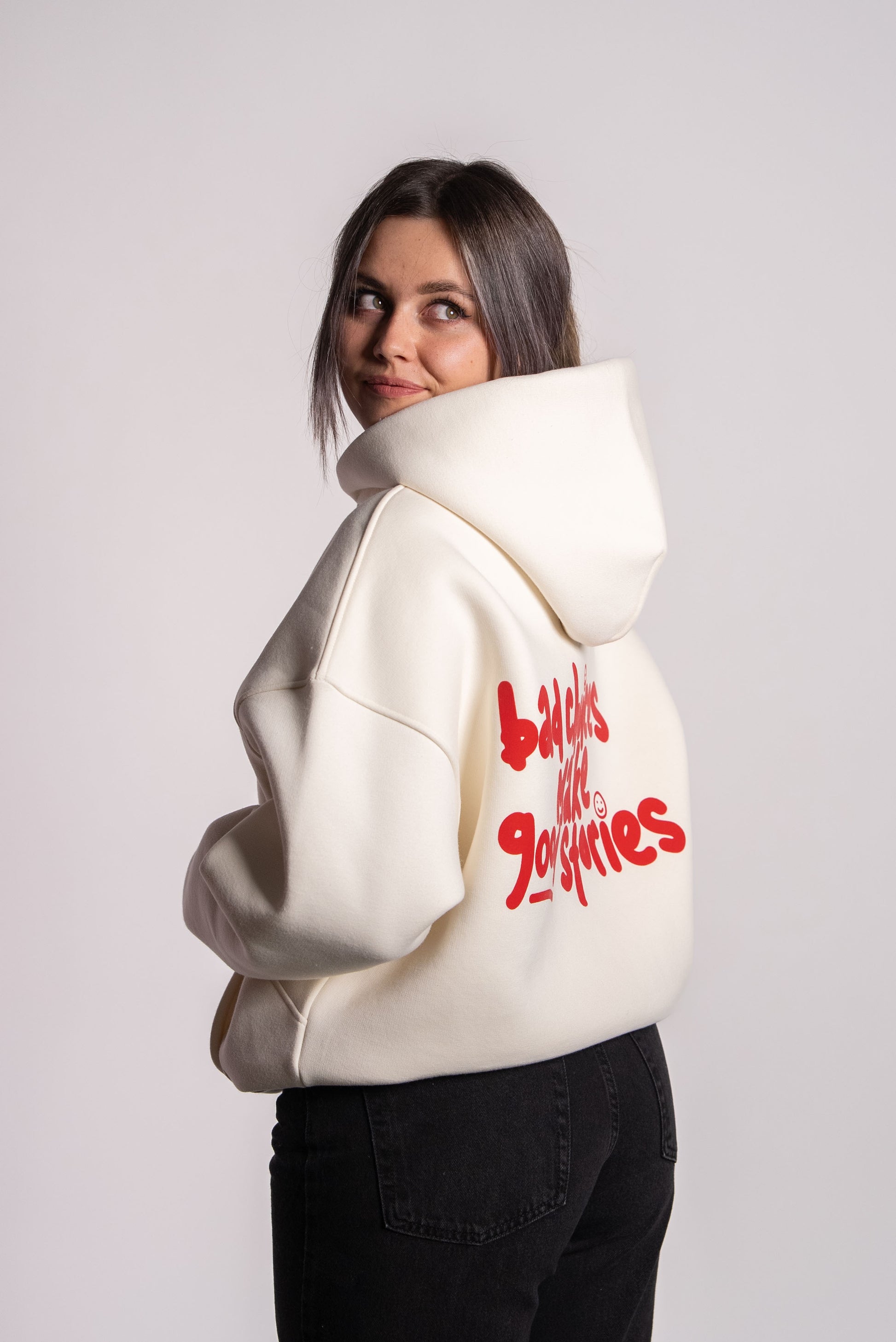 Nahaufnahme von Sophie, die einen cremefarbenen Hoodie trägt. Der Blick ist über die Schulter nach hinten gerichtet. Auf dem Rücken steht in rotem, verspieltem Schriftzug: „bad choices make good stories“. Sophie ist 169 cm groß und trägt Größe M.