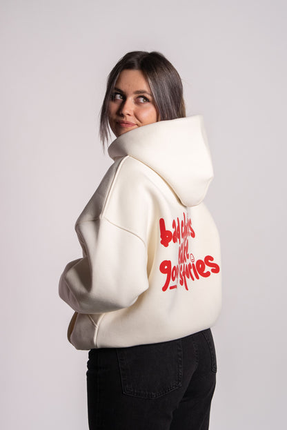 Nahaufnahme von Sophie, die einen cremefarbenen Hoodie trägt. Der Blick ist über die Schulter nach hinten gerichtet. Auf dem Rücken steht in rotem, verspieltem Schriftzug: „bad choices make good stories“. Sophie ist 169 cm groß und trägt Größe M.